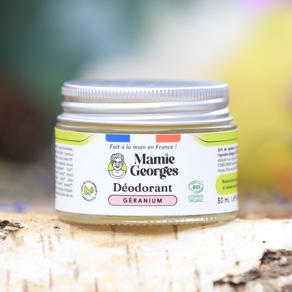 Pot de déodorant Géranium de Mamie Georges sur une bûche de bouleau, orchidées roses en arrière-plan