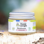 Pot de déodorant Géranium de Mamie Georges sur une bûche de bouleau, orchidées roses en arrière-plan