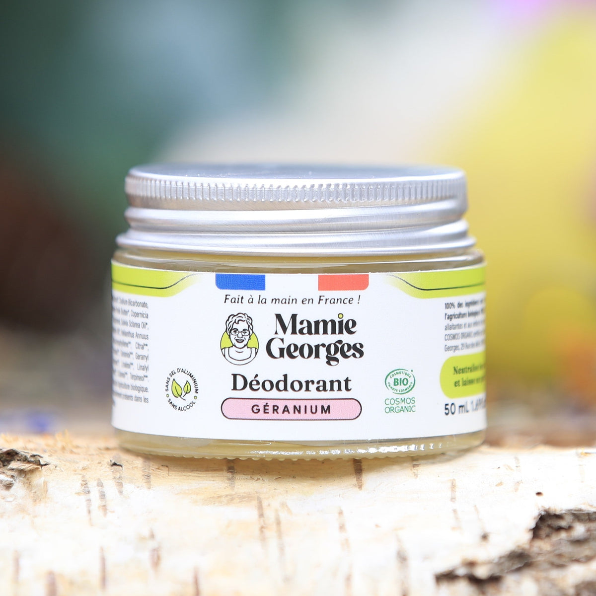 Pot de déodorant Géranium de Mamie Georges sur une bûche de bouleau, orchidées roses en arrière-plan