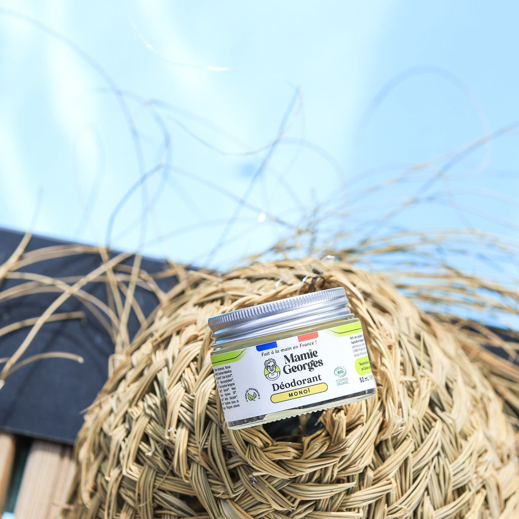 Pot de déodorant Monoï sur un chapeau de paille, ciel bleu en fond