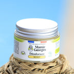Pot de déodorant Monoï de Mamie Georges posé sur un panier de paille, sous le ciel bleu