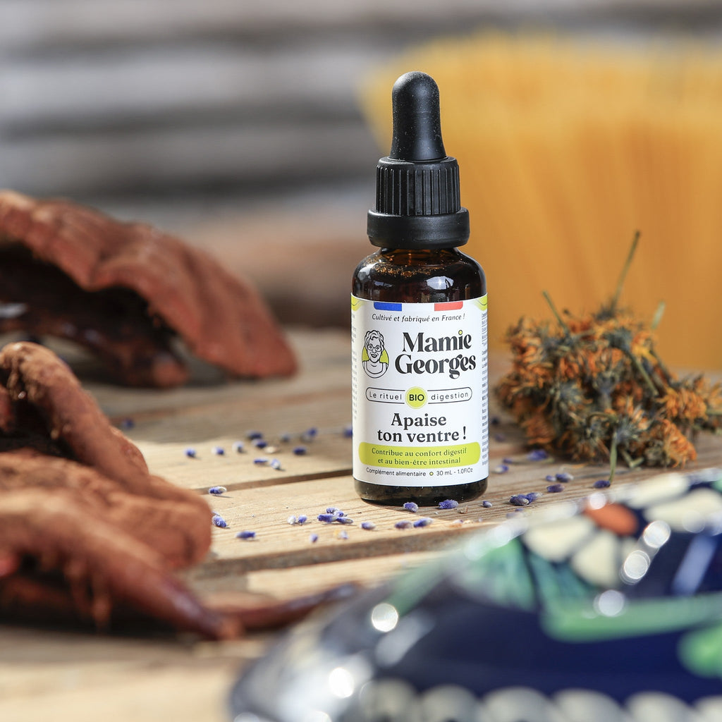 Flacon Apaise ton ventre ! sur une table en bois, entre reishi, calendula et un plat émaillé