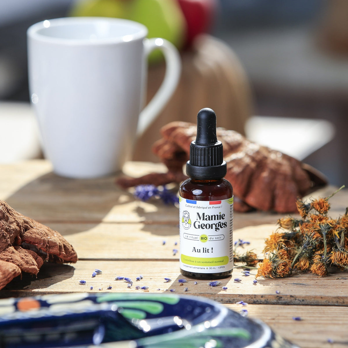 Flacon Au lit ! sur une table en bois, près d'une tasse blanche, de reishi et de fleurs de calendula